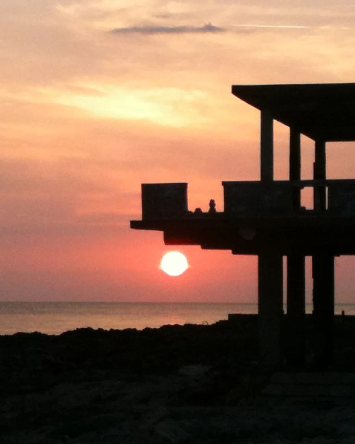 The sun dropping to the horizon behind a cliff top structure on Negril's West End, with the sea below